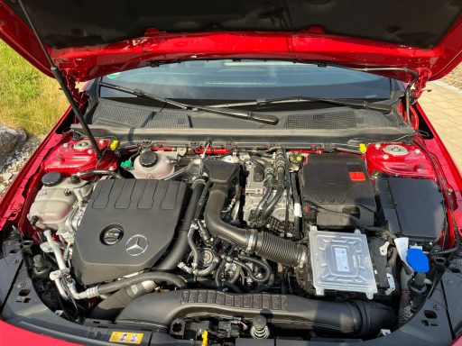 Motorraum eines roten Autos mit sichtbarem Motor und Zubehörteilen.