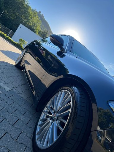 Schwarzes Auto in der Seitenansicht mit glanzvollem Rad und sonnigem Hintergrund.