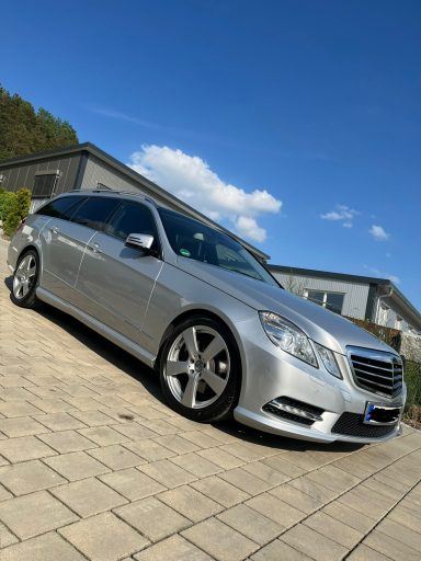 Silberner Mercedes-Benz Kombi parkt auf gepflastertem Grundstück vor einem modernen Gebäude.