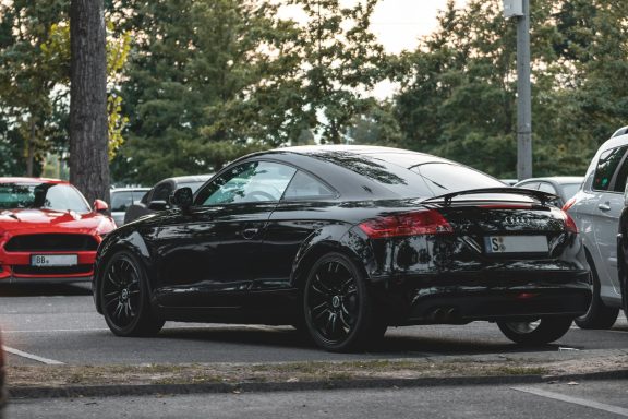Schwarzes Sportcoupé parkt auf einem Parkplatz, umgeben von anderen Autos.