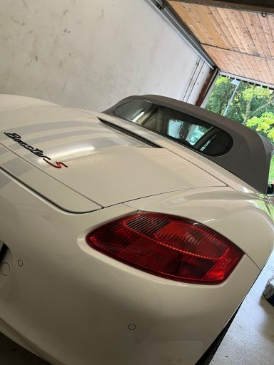 Ein weißer Sportwagen mit offenem Dach steht in einer Garage.