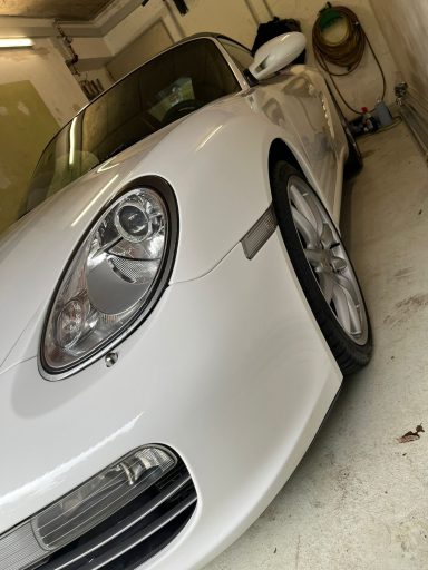Weißer Sportwagen steht in einer Garage mit glänzenden Felgen und reflektierenden Oberflächen.